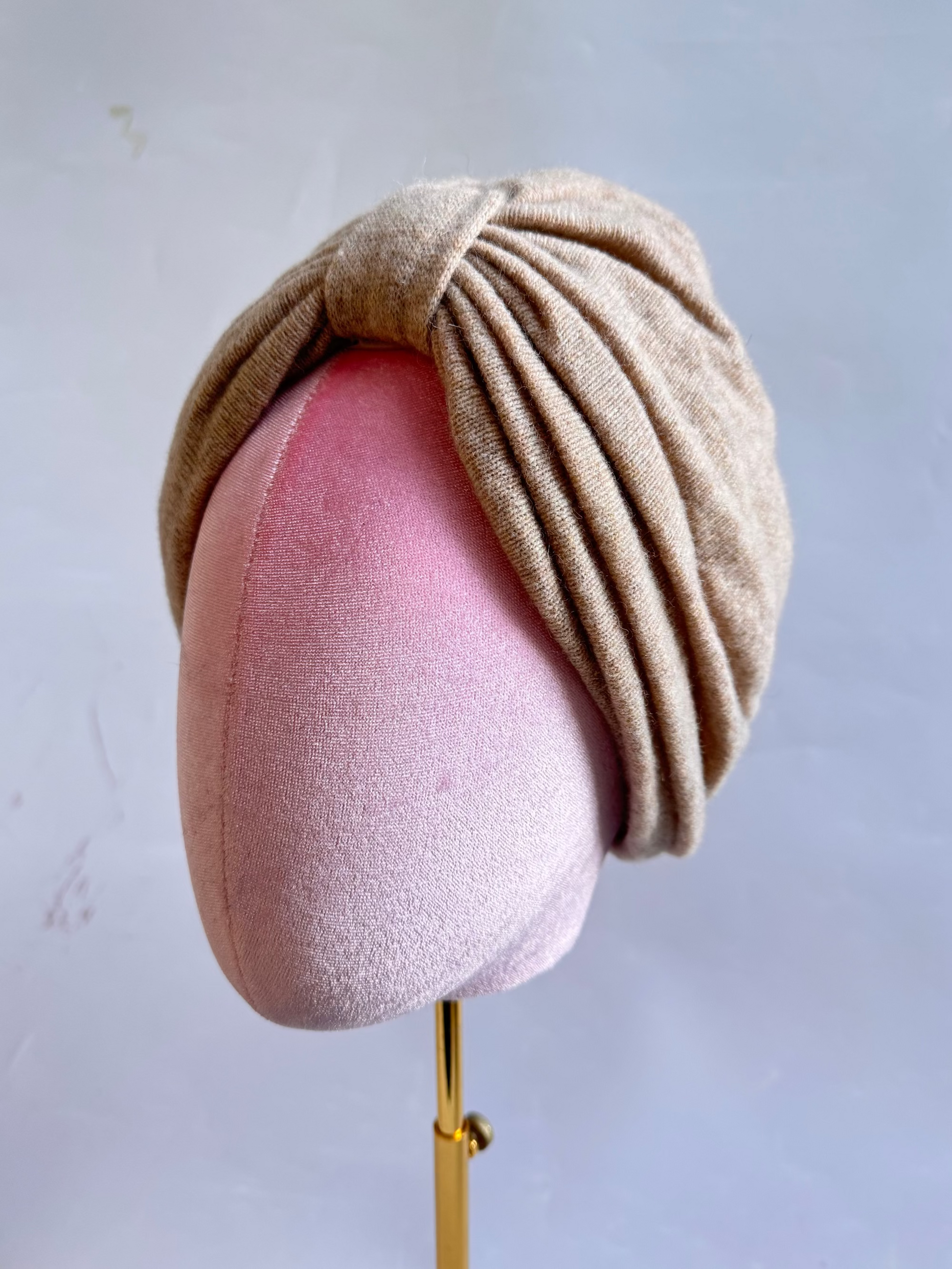 Beige wool turban hat on a mannequin head with a plain background