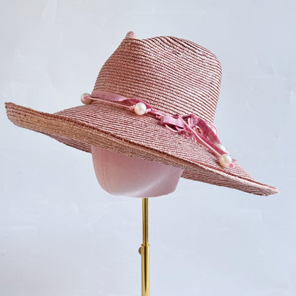 Pink straw hat with pearl accents on a mannequin head against a light gray background